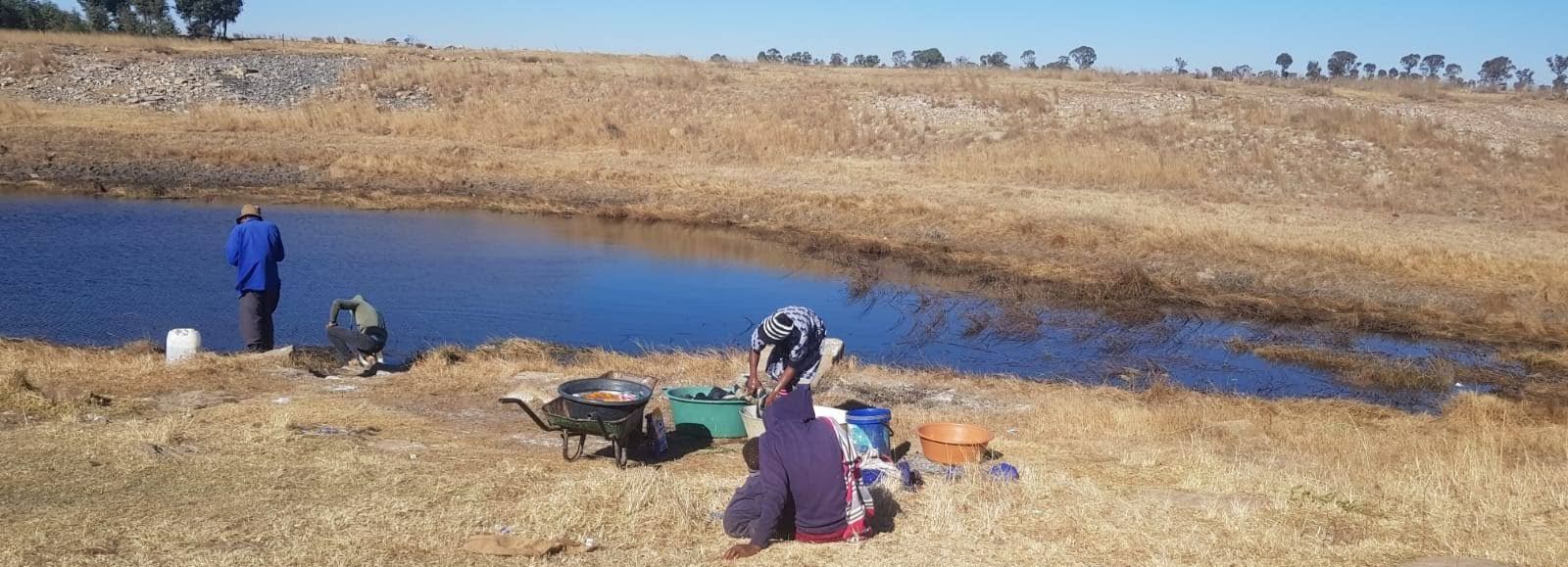 Men collect water at a pond while a lady washes her clothes